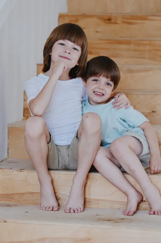 Two happy boys sitting on wooden stairs, enjoying each other's company. Their joyful expressions illuminate the playful atmosphere of childhood friendship.