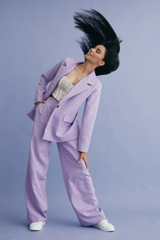 stylish woman in lavender suit with flowing hair poses confidently against light blue background, showcasing modern fashion and dynamic movement in studio setting
