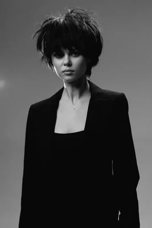 Black and white portrait of a young woman with short hair in dark clothing, expressing calm and confidence in a studio setting.
