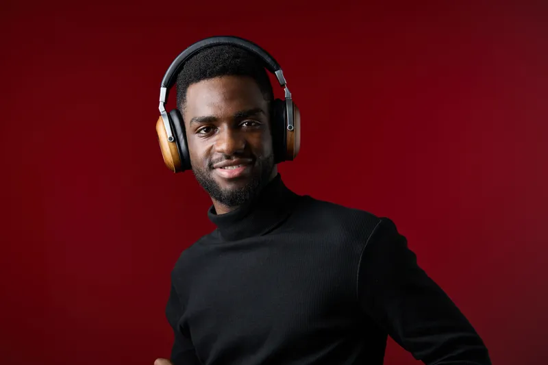 Young Black man with headphones smiling against a red background, showcasing modern fashion and cozy ambiance, ideal for music and lifestyle concepts