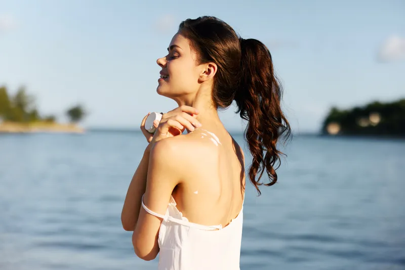 Relaxed young woman enjoying sunshine at the beach wearing white dress with natural makeup and tied hair, summertime serenity and calm outdoor moment.