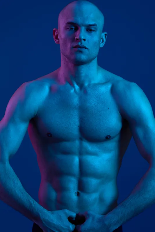 Athletic man with a confident expression, showcasing a strong physique against a blue background, highlighting the beauty of strength and determination.