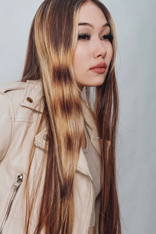 Young woman with long straight hair wearing a light jacket, looking sideways with a neutral expression in indoor studio. Face, hairstyle, fashion and portrait photography.