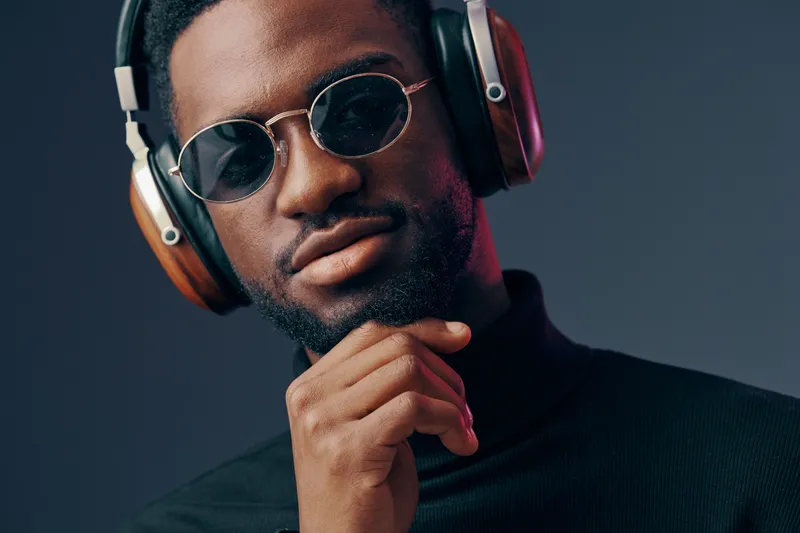 Stylish man with headphones in sunglasses, exuding confidence against a dark background, showcasing modern urban fashion and music culture in a vibrant color palette
