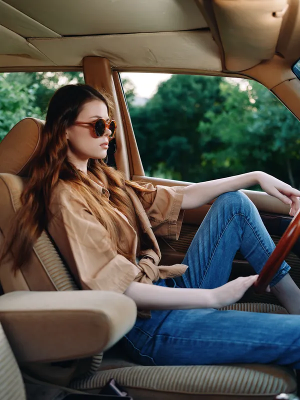 Stylish woman in casual outfit seated in a vintage car, showcasing a relaxed vibe and soft sunlight with a focus on nature-inspired colors.