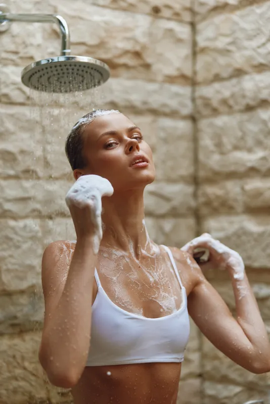 Woman washing body with foam under outdoor shower, natural stone background, skincare routine, healthy skin, fresh and rejuvenating moment.