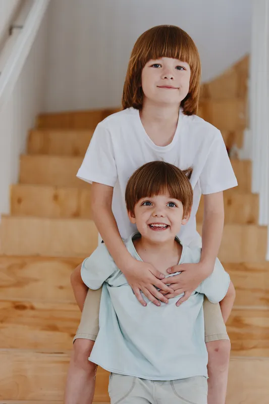 Playful children enjoying their time together, smiling and dressed casually, on wooden stairs in a bright indoor setting, perfect for family-themed visuals.