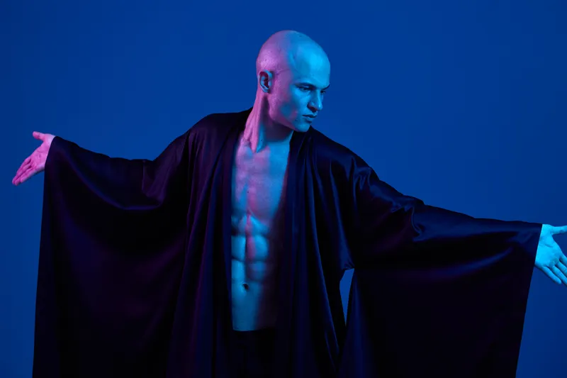 A striking image of a man wearing a flowing black garment, showcasing confidence against a vibrant blue background. This black and white composition captures elegance and strength.
