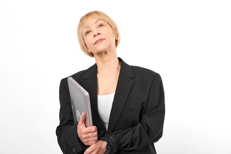 Elderly woman in business blazer holding tablet, thinking on white office background, focused portrait, technology and communication concept, soft studio light, calm mood
