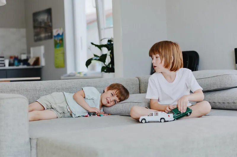 Two young children playing together on a sofa, featuring a boy with toys and a smiling girl. The cozy home setting adds warmth and joy to the scene.
