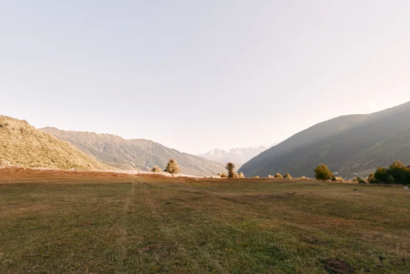 Meadow valley mountains grass landscape hills sky sunrise captured in warm morning light over a wide open expanse, peaceful rural scenery with distant ridges and soft horizon.