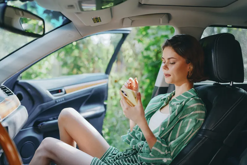 Car, woman, interior scene shows a calm woman seated in the front seat, examining a phone with a gentle focus, preparing for a journey and enjoying a quiet moment.