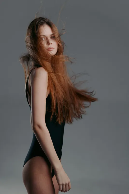 Young woman with long flowing hair wearing black bodysuit against grey background