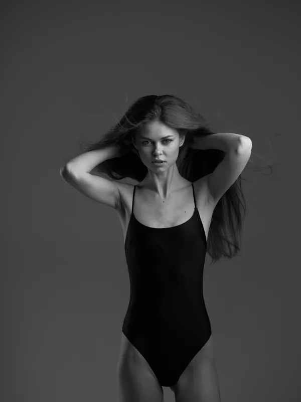 black and white portrait of a slender woman in a black swimsuit with intense expression and flowing hair