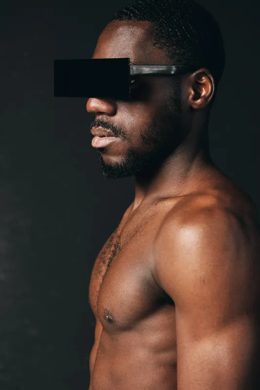 African man with dark skin and muscular body wearing futuristic black visor in creative conceptual visual style on dark background. Portrait of confident male model with bare torso.