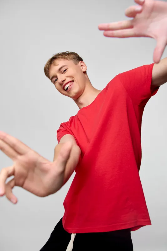 Dynamic movement of a cheerful young man reaching toward the camera in a red shirt, capturing energy, action, and expressive youth in a studio setting