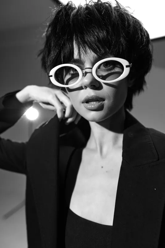 Black and white portrait of stylish woman wearing white sunglasses and black blazer with confident expression