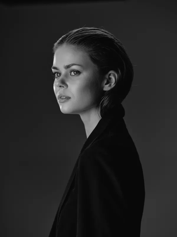 Young woman in black and white portrait with serious expression looking sideways in dark studio lighting.