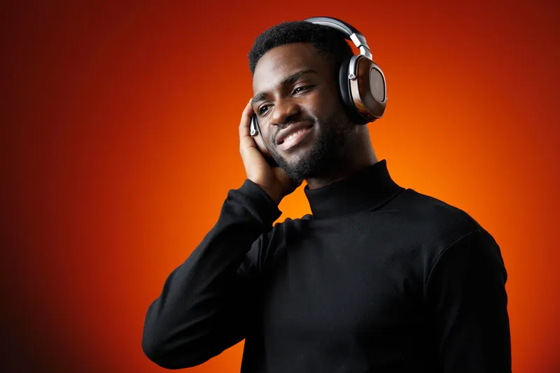 Young Black man enjoying music with headphones against an orange background, radiating happiness and relaxation during a vibrant listening experience