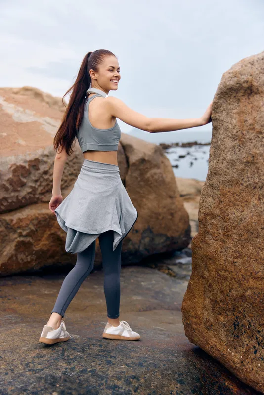 Athletic woman in gray workout apparel poses by the beach, showcasing confidence and health, emphasizing outdoor fitness and active lifestyle