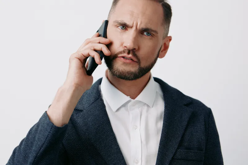 A business professional man speaks on a mobile phone, expressing intensity and focus, set against an isolated colored background to emphasize urgency and clear communication.