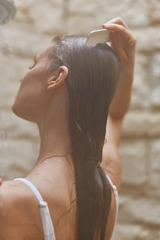 woman combing wet hair under natural light, close-up of back view, smooth dark hair, relaxed morning routine, soft neutral background
