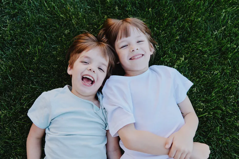 Happy children lying on green grass, enjoying a sunny day outdoors, sharing laughter and joy, creating cherished memories in a playful atmosphere.