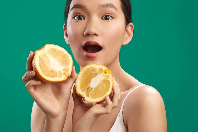 asian woman holds lemon halves in a vibrant studio shot, smiling with a bright expression, showcasing fresh produce and a lively, refreshing mood.