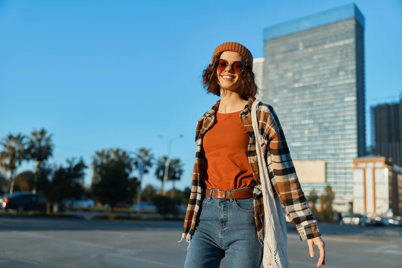 Woman smiling urban casual walking sunglasses beanie jeans in a golden hour scene, candid lifestyle portrait with authenticity, joyful mindful living and emotional storytelling mood.