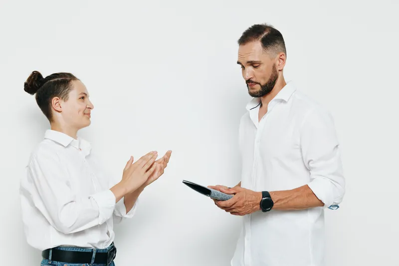A professional businessman stands on a white background, exuding confidence and calm energy while delivering ideas to a colleague, with poised posture and engaging expression.