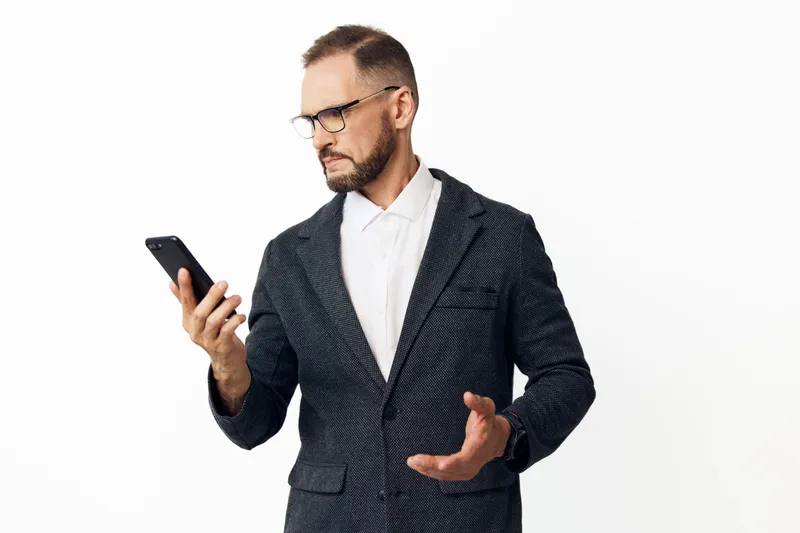 A professional businessman stands with a poised stance, checking a smartphone on an isolated colored background, conveying focus, confidence, and thoughtful emotion.