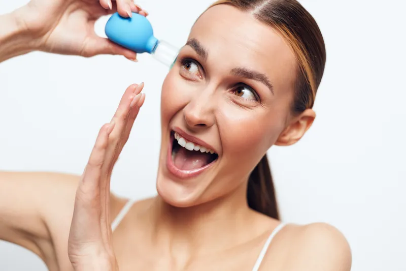 Young woman with clear skin applies blue facial cleanser with dropper bottle smiling and looking happy isolated on white background skincare beauty routine concept