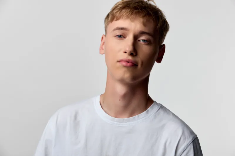 Young man wearing a white t shirt stands in a studio, calm expression, soft lighting, clean background, thoughtful mood, minimalist fashion composition