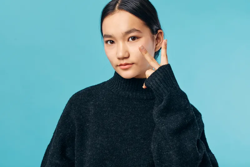 Young woman applying cream on face with finger for skincare routine. Beauty, health and personal care concept with natural look and clean skin on blue background.