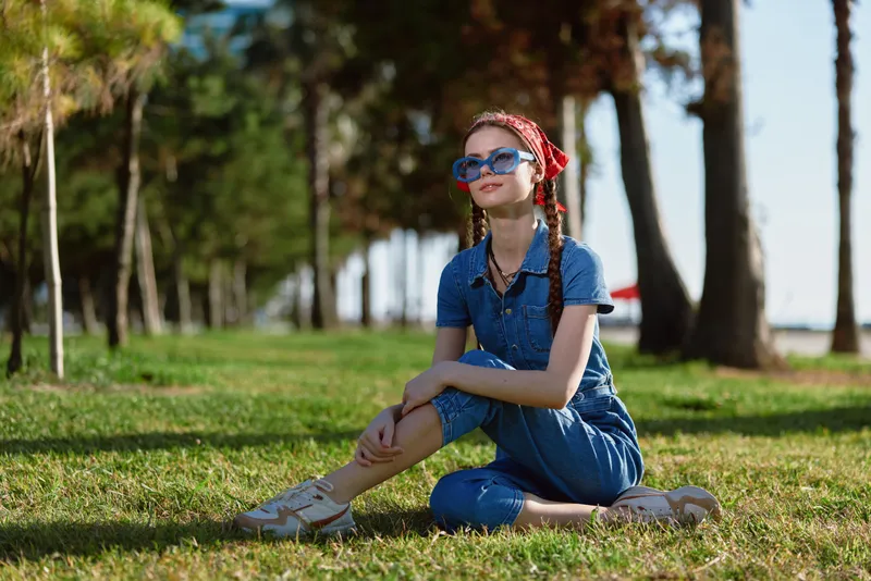 Lifestyle woman wearing modern boho-western denim street style sitting on grass outdoors, film color effect enhancing relaxed and stylish mood in natural light.