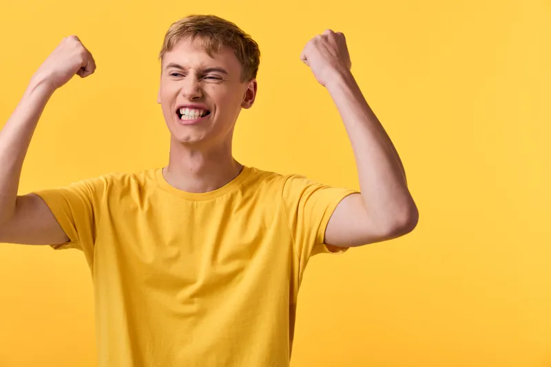 Joyful man in yellow shirt raises his arms in triumph against a vibrant backdrop, conveying motivation, energy and celebration suitable for success, fitness and positive mindset campaigns