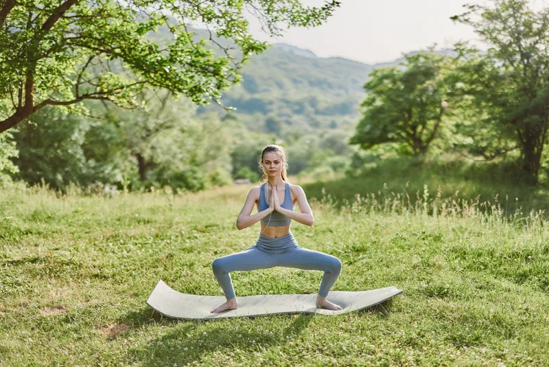 Young woman practicing yoga outdoors in a serene green landscape, wearing blue activewear, exuding calmness and focus, perfect for wellness and fitness concepts