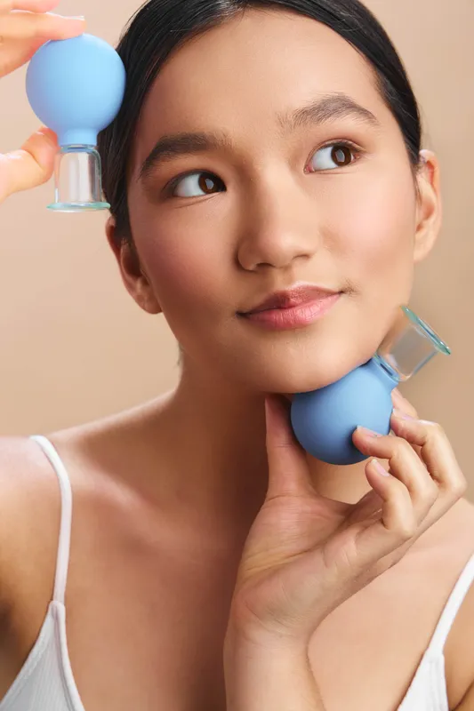 asian woman uses silicone facial cleansing devices in a bright home setting, gently massaging the skin with dual tools to promote a luminous, healthy complexion and relaxing selfcare ritual.