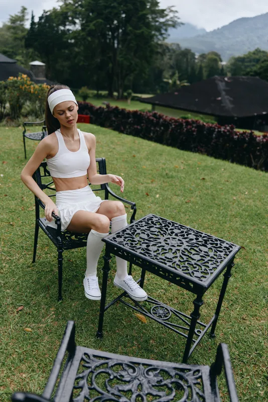 A young woman in sporty attire enjoys a serene moment outdoors, wearing a white crop top and skirt, showcasing a healthy lifestyle