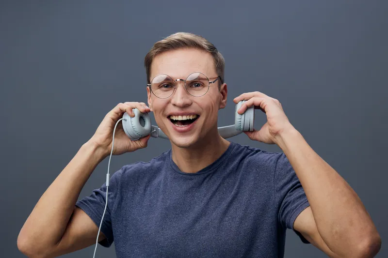 happy smiling young man wear glasses hold headphones near ears enjoy music lifestyle concept isolated on grey background studio portrait digital detox headphones