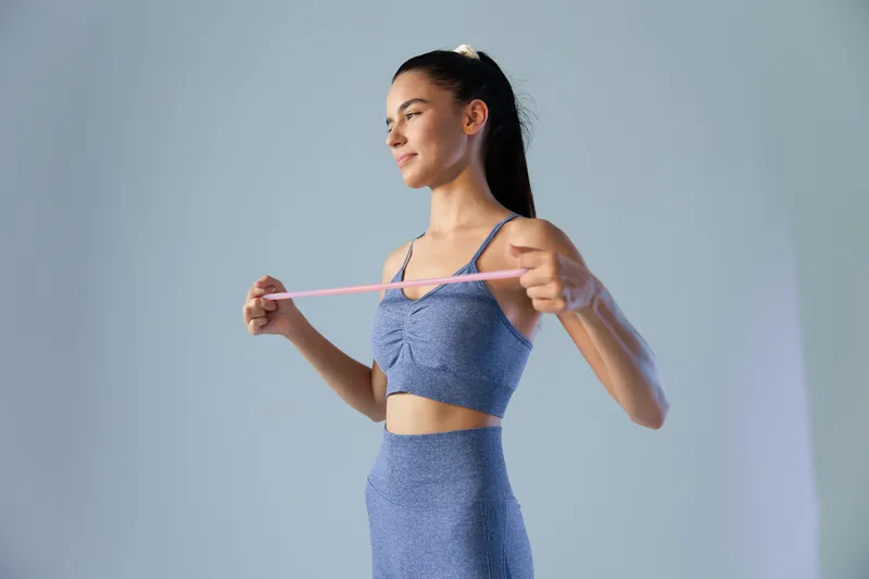 fit woman exercising with resistance band wearing blue sportswear, focused and calm, isolated light background, indoor fitness training, woman sport fitness concept