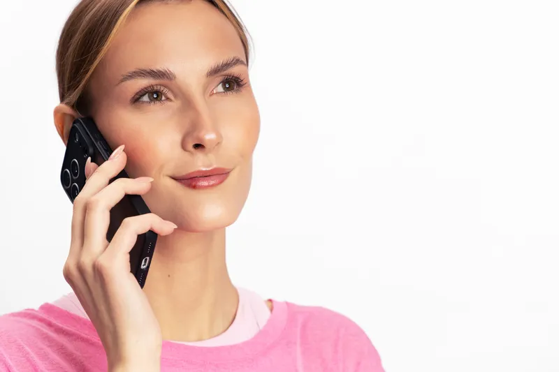 Young woman in pink sweater talking on smartphone, looking thoughtful. Close-up portrait on white background. Concept for communication, technology, and casual lifestyle.