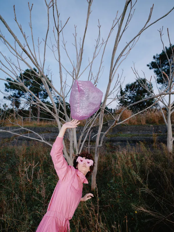 Girl in a pink dress releases a pink lantern outdoors among bare trees, capturing a calm celebration moment with nature, gentle wind and soft evening light for a dreamy scene