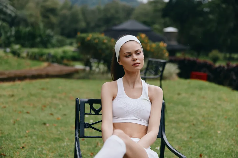 Young woman in a sports outfit relaxing outdoors, exuding calmness and wellness in a green garden, emphasizing healthy living, fitness, and relaxation