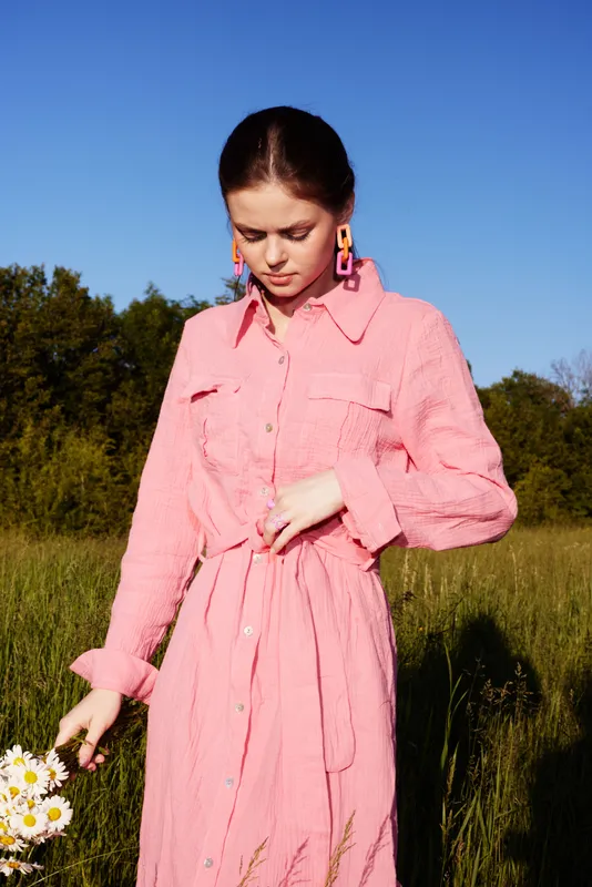 Young woman in a pink linen dress holding flowers in a sunny meadow, embodying summer vibes and tranquility