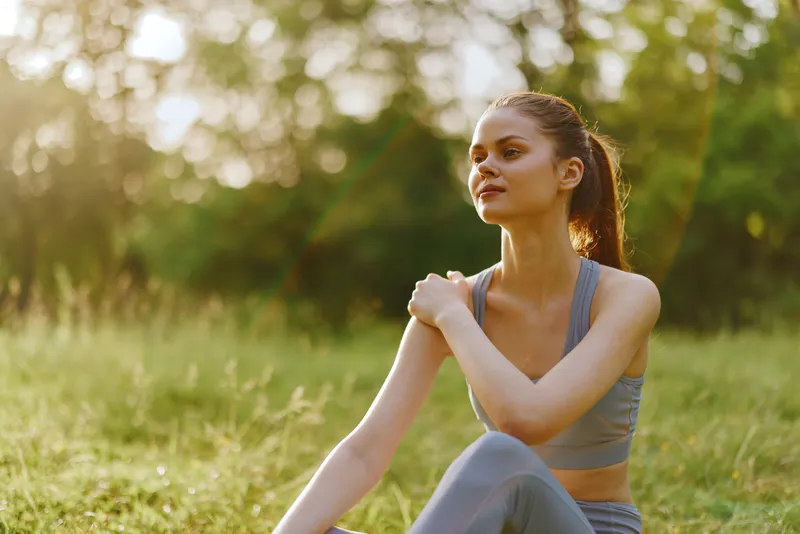 Young fitness model in sportswear enjoying nature, exuding confidence and tranquility in a sunlit park setting Keywords exercise, relaxation, outdoor