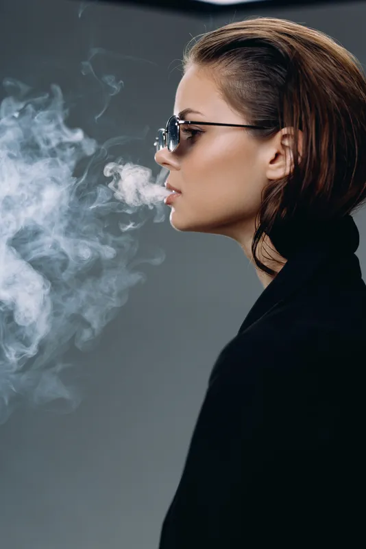 Profile of a woman wearing sunglasses exhaling smoke, stylish and calm atmosphere.