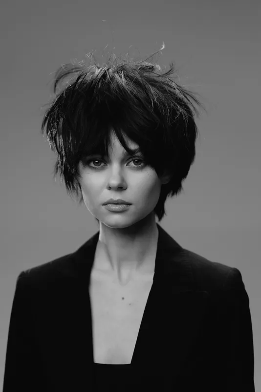 Black and white portrait of a young woman with short messy hair in a dark jacket.