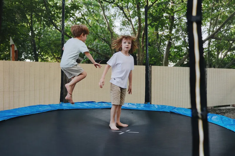 Two joyful boys play together on a trampoline, enjoying a sunny day outdoors, expressing happiness and excitement in their playful moment.