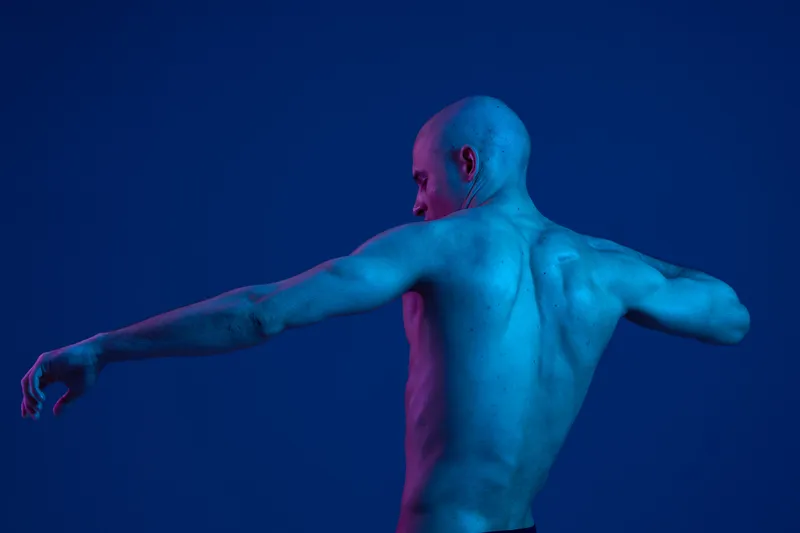 Athletic man posing in dramatic blue and pink lighting, showcasing his toned back. This unique black and white image highlights strength and artistic expression.